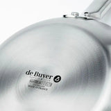 A close-up of the shiny bottom of a De Buyer Alchimy Saucepan shows the logo and text indicating this 1.05 qt stainless steel saucepan is made in France, suitable for all stovetops including induction, embossed in black on the metal surface.