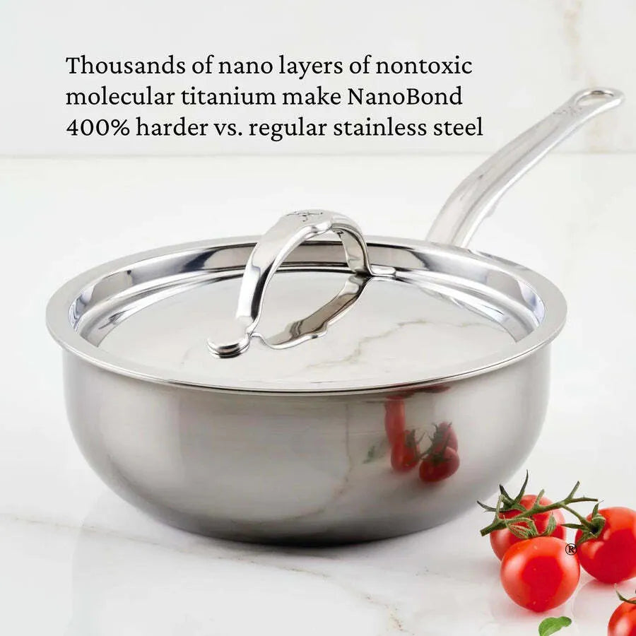 A shiny Hestan NanoBond Saucier pan, 2.0qt with a lid and curved handle sits on a white surface beside cherry tomatoes. JB Prince text above details the nontoxic titanium NanoBond coat, 400% harder than regular stainless steel.