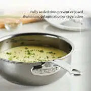 A Hestan Nanobond Saucier pan, 2.0qt, filled with creamy soup and garnished with chopped herbs sits on a white countertop. The text above reads: "Fully sealed rims prevent exposed aluminum, delamination or separation.