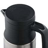 A stainless steel beverage server with vacuum insulation features a black plastic lid and handle. The lid has a small spout and the word “POUR” with an arrow, indicating the direction. The carafe is viewed from a slightly elevated angle.