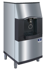 A commercial vending ice dispenser in stainless steel and black, featuring a modern, angular design with a touchless lever for hygienic use. It stands on four short legs and boasts a 120-lb capacity, with a distinctive blue-and-white logo on the front.