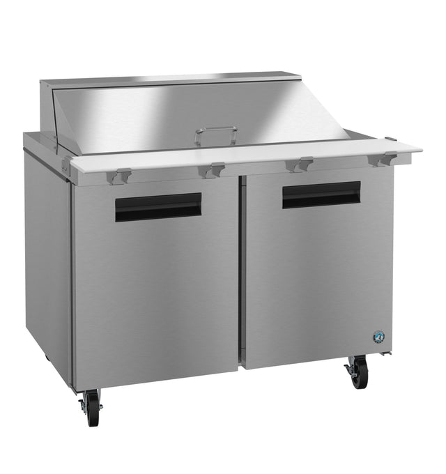A stainless steel mega top refrigerator with two black-handled doors, a white prep surface, and an angled lid. Four caster wheels provide mobility, making it ideal for use as a sandwich or salad prep station in a professional kitchen.
