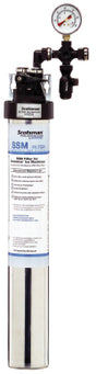 Tall cylindrical water filter assembly with a labeled cartridge at the bottom, black top cap, pressure gauge, and connected piping at the top. The gauge displays pressure, and the “SSM” by ScaleGard is intended for water treatment and antimicrobial protection.