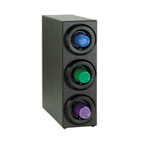A black rectangular coffee pod holder stands upright, resembling a compact Cup Dispenser Cabinet, with three circular slots on the front—each housing a blue, green, or purple coffee pod—set against a plain white background.