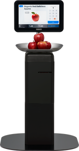 A digital self-serve scale, like the Hobart FS-200, displays Organic Red Delicious Apples with a price and keypad. On a scale below the screen, five red apples sit in a shallow metal bowl on a sleek black platform.