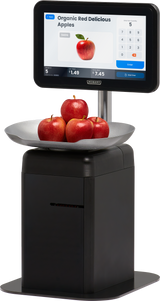 A digital touchscreen scale displays “Organic Red Delicious Apples” with a price and image. Four red apples rest in a metal bowl atop the self-serve scale, which features a black base and a touchscreen for item selection and checkout.