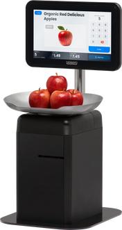 A digital touchscreen scale displays “Organic Red Delicious Apples” with a price and image. Four red apples rest in a metal bowl atop the self-serve scale, which features a black base and a touchscreen for item selection and checkout.