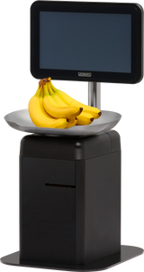 A bunch of bananas sits on the weighing tray of a modern black self-serve scale with a large display screen above it, set against a plain white background. The screen is blank, and the scale is marked with the brand Hobbit.