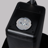 Close-up of a black rectangular device, possibly a Hobart FS-30V table-top scale, with a circular metal component on top secured by four screws. Four small metal elements are visible on the plate, all encased in rounded plastic against a light gray background.