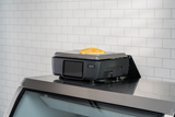 A black flat-top griddle with a customer display sits on a counter, cooking a sunny-side-up egg. The background features white subway tile, and the griddle has a digital display and side vents.