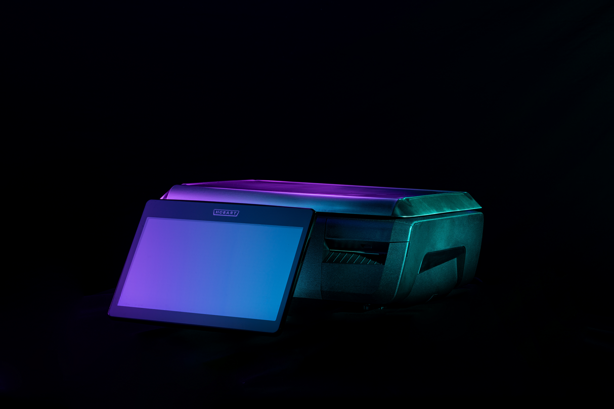 A GTI Scale/Printer and a digital tablet are placed together on a dark background. Both devices are illuminated with soft blue and purple lights, giving a modern, high-tech look. The tablet, serving as an operator display, is blank and angled in front of the printer.