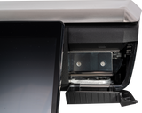A close-up of a GTS Printer point-of-sale terminal shows the edge of a touchscreen on the left and the receipt paper compartment with a metal holder and partially exposed roll inside on the right. The plastic cover is lifted, revealing internal parts.