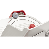 Close-up of a Berkel slicer, focusing on the 12 inch carbon steel knife with sharpening stones above it. The design features red, gray, and metallic components, with a protective guard partially covering the cutting edge.