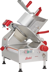 A silver and red Berkel gravity feed slicer with a 12 carbon steel knife, tilted blade, food carriage, safety guard, control knobs, and labeled buttons. The machine stands on four rubber-tipped feet and displays the Berkel logo on its side and front.