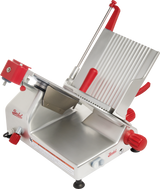 A commercial-grade manual gravity feed slicer with a silver metal body, red knobs and handles, tilted grooved platform for holding food, carbon steel knife, large blade guard, and sturdy black feet for stability is shown on a white background.