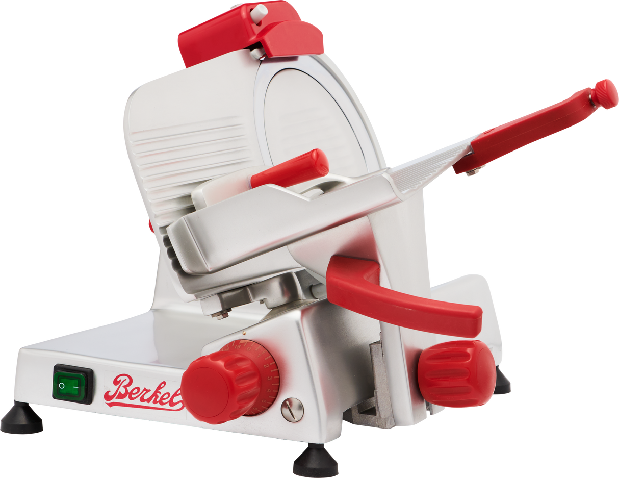 A silver Berkel slicer with red accents—including knobs, handle, and logo—features a circular blade, adjustable thickness dial, safety guard, and green on/off switch. This gravity feed slicer is positioned at an angle for easy use.