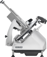 A metallic Hobart Heavy Duty Meat Slicer is shown in side view. The machine has a tilted blade, adjustable handle, and supportive base with black feet. The Hobart logo is visible on the lower front panel. The slicer is clean and modern in design.