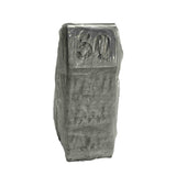 A stack of rectangular, gray TableCraft number tent set objects wrapped tightly in plastic, with 50 embossed on the visible top surface. The clear, crinkled wrapping reveals the stainless steel shapes and numbers beneath against a plain white background.