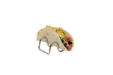 A soft taco filled with shredded cheese, lettuce, avocado, tomatoes, black beans, and possibly sour cream sits upright in a Taco Taxi Server—an elegant, stainless steel holder that's also dishwasher safe—against a plain white background.