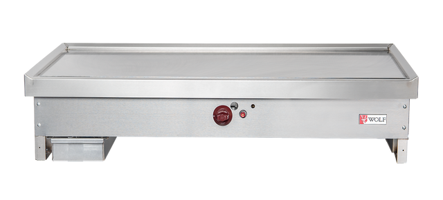 A stainless steel teppanyaki griddle with a flat cooking surface, red center control knob, indicator lights, left-side grease trap, and Wolf TYG60C_LP branding on the right. The rectangular design suits any commercial kitchen griddle setup.