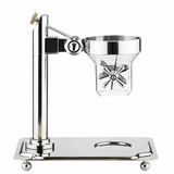 A polished metal citrus juicer by TableCraft stands on a rectangular base with rounded feet. It features a vertical column, a funnel-shaped juicing cup, a paddle handle, and a spout below. The design is modern and shiny with clean, reflective surfaces.