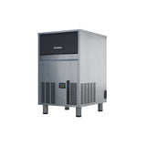 A stainless steel undercounter ice maker by Scotsman stands on four legs. The front panel features black vents, control buttons, and a display. The upper section has a black lid with the Scotsman logo and produces gourmet cube ice. Modern, industrial design; white background.