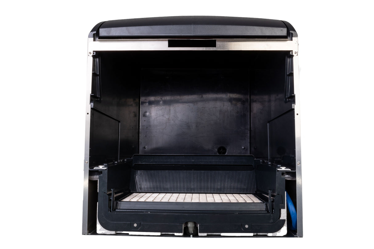 A close-up view of an open, empty black cube style ice maker with a grid-patterned tray at the bottom and a rectangular opening at the top; the background is white.