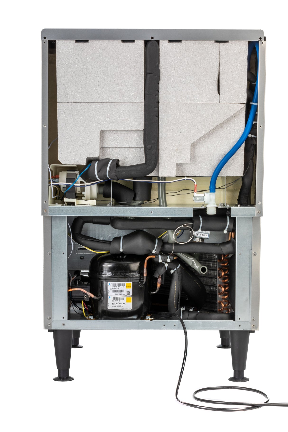 A Scotsman Ice Maker with the front panel removed reveals insulated foam panels, copper tubing, a black compressor, various wires, and controls inside a metal frame on four legs. A power cord hangs from the bottom section.