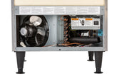 The image shows the lower back panel of an Undercounter Ice Maker with its cover removed, exposing internal components: a large black fan on the left, copper coils and wiring in the center, insulation, warning labels, and four black adjustable legs.