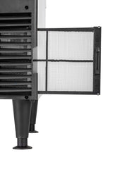 Close-up of a self-contained condenser air purifier standing on four legs, with its front filter panel open to reveal a white mesh filter inside a black frame. The appliance features vented slots and a clean, modern design.