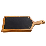 A rectangular wood serving tray with a handle and a hole for hanging, featuring a black, slate-like inset in the center secured by four brass screws at the corners. The board is isolated on a white background.