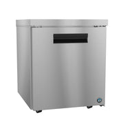 A commercial ADA Compliant stainless steel refrigerator with a single solid door, recessed black handle, and small wheels for mobility. The front panel features a round blue and white manufacturer logo in the lower right corner.
