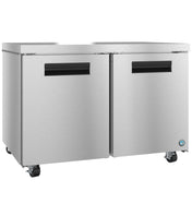 A commercial stainless steel undercounter freezer with two doors, black horizontal handles, and four caster wheels for mobility. The smooth metallic surface features a small blue logo on the lower right corner.
