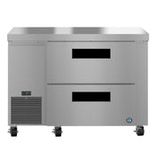 A Hoshizaki stainless steel undercounter refrigerator with two front drawers, a ventilation grate, digital display on the lower left, four caster wheels, and a blue logo near the bottom right corner.