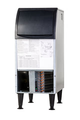 A commercial undercounter ice maker with a black top lid, white body, and visible internal components including wiring, coils, and a control panel. The front panel displays technical information and diagrams. The unit stands on four black legs.