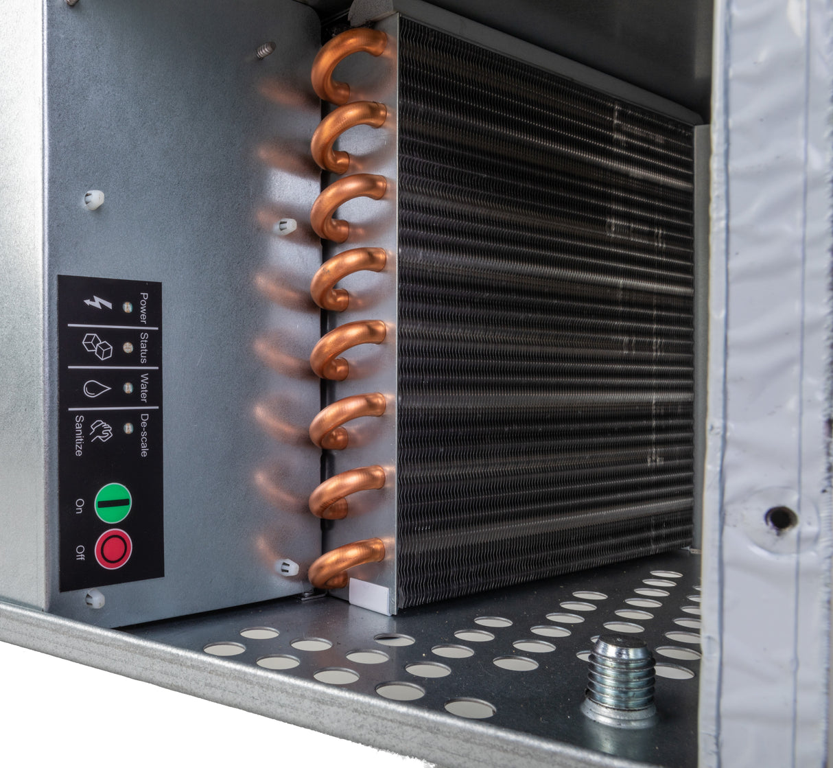 Close-up of an industrial HVAC evaporator coil with copper tubing and aluminum fins, resembling components in an undercounter ice maker. A control panel with status indicators sits on the left, while the perforated metal base features a protruding bolt.