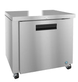 A stainless steel Energy Star undercounter refrigerator with a single front door, black recessed handle, lock, flat top, and four caster wheels for mobility. The brushed metal finish features a small blue logo on the lower right corner.
