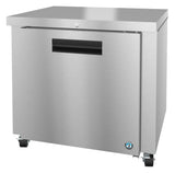 A stainless steel undercounter refrigerator on wheels, featuring a single front door with a recessed black handle, a lock above the handle, and a small blue logo in the lower right corner. The surface has a brushed metal finish.