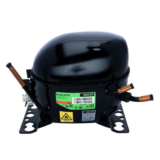 A black, oval-shaped Empura Parts compressor with copper tubes extending from its sides. It sits on a flat metal base with mounting holes. A green and white label and a yellow caution sticker are visible—ideal for Empura ice machines.