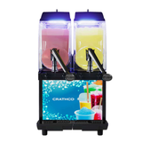 A dual-tank Crathco I-PRO 2M frozen granita dispenser with blue lighting, holding pink and yellow slush drinks. Each tank has a push handle for dispensing, and the lower front showcases colorful drinks in cups and the CRATHCO brand name.