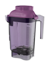 A transparent purple 48 oz Vitamix blender container with measurement markings, BPA free, featuring a handle and a purple lid with Spanish text. Sharp metal blades sit at the bottom, all photographed on a white background.