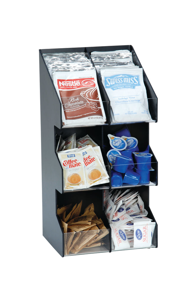 A black condiment organizer sits on the countertop, holding packets of Nestlé hot chocolate, Swiss Miss cocoa, Coffee-mate creamer, blue liquid creamers, sugar, and Sweet’N Low—all neatly separated in clear compartments.
