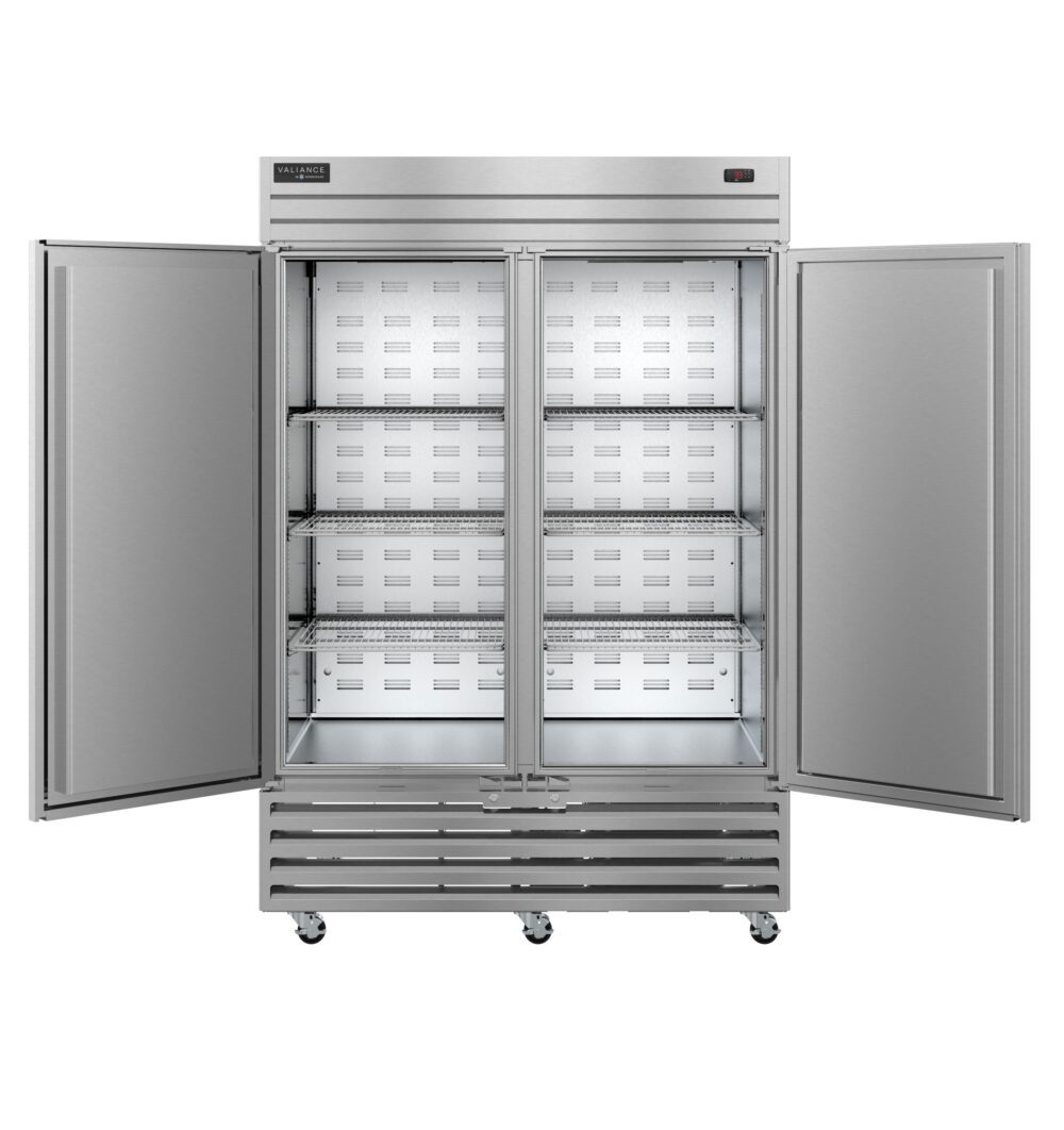 A large Valiance Series two-section refrigerator with stainless doors stands on wheels, its double doors open to reveal three adjustable metal wire shelves inside. The spacious interior is empty, and a digital control panel is visible at the top right.