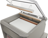 A close-up of a single chamber Vacuum Packaging Machine with its transparent lid open, revealing the sealing bars and a white rectangular insert inside the stainless steel chamber. The machine features a clean, modern design.