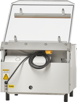 A white single chamber Vacuum Packaging Machine with a hinged, transparent lid propped open. A thick black power cord with a yellow plug hangs at the front. “GAS” and warning labels are visible on its metallic, utilitarian body with short legs.