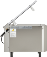 A stainless steel Berkel single chamber vacuum packaging machine is shown side-on with its lid open. The machine features warning labels, simple black legs, and a transparent lid attached with metal arms at an angle.