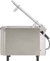 Side view of a single chamber vacuum packaging machine with its lid open at an angle. The stainless steel device features four black legs, a rectangular chamber, visible hinges and wiring for gas flush on the right side connecting the lid to the base.