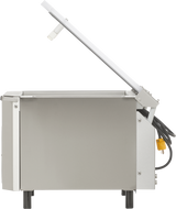 A Berkel single chamber Vacuum Packaging Machine, crafted in stainless steel, features a rectangular body on four short black legs. The hinged lid opens to reveal the inner compartment, while a black power cord and yellow plug extend from the back.