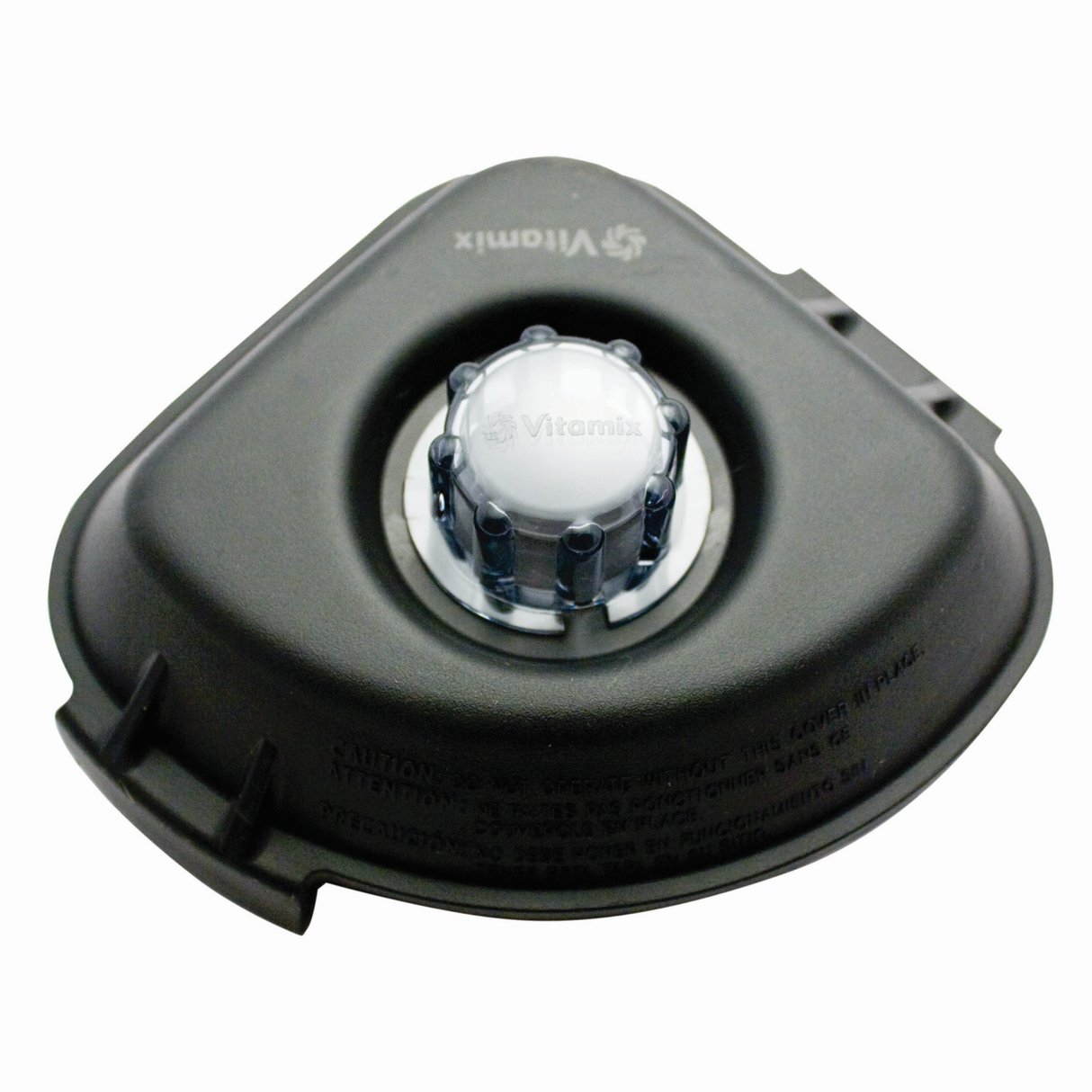 A black Vitamix lid for Advance containers, featuring a clear plastic removable center cap and rubber plug, is shown from above on a white background. The Vitamix logo is embossed near the cap, with cautionary text printed along the edge.