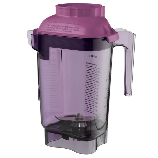 Clear plastic Tritan container blender pitcher with measurement markings, a handle, and a purple lid. This BPA Free Vitamix blender container is transparent with a slight purple tint, metal blades at the bottom, and multilingual safety instructions on the textured lid.